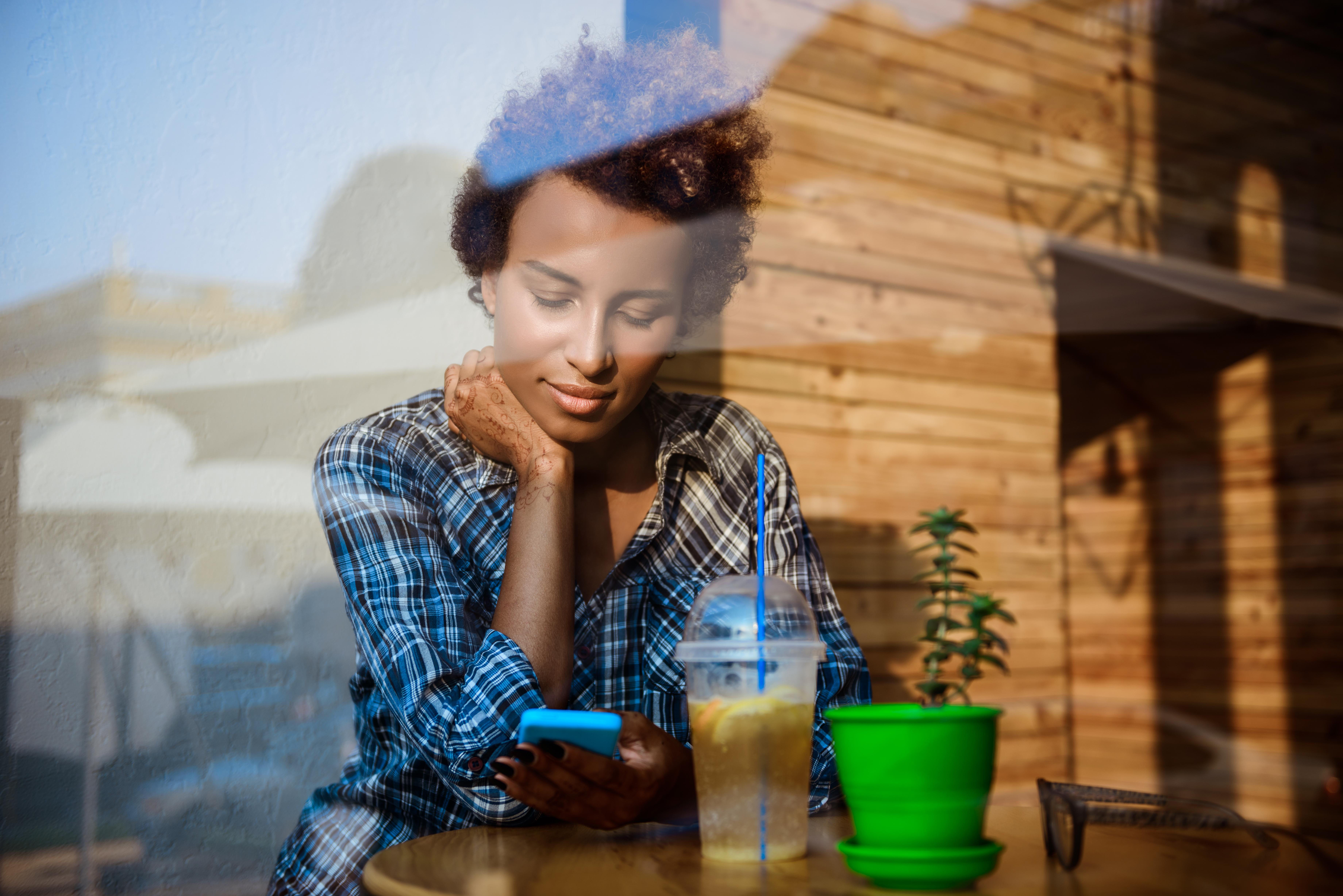 beautiful-african-girl-smiling-looking-phone-sitting-cafe-shot-from-outside